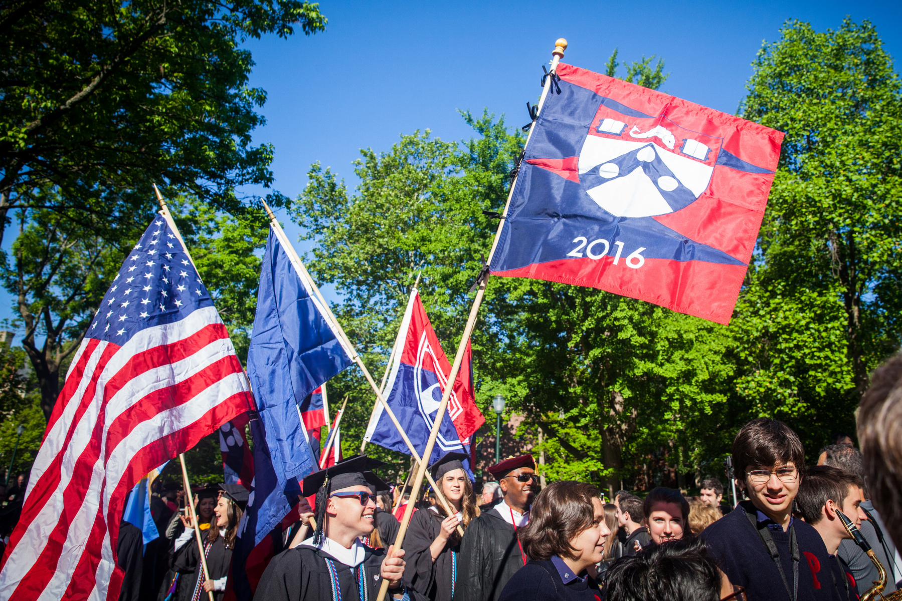 graduates carrying flags labeled with 2016 and the penn shield