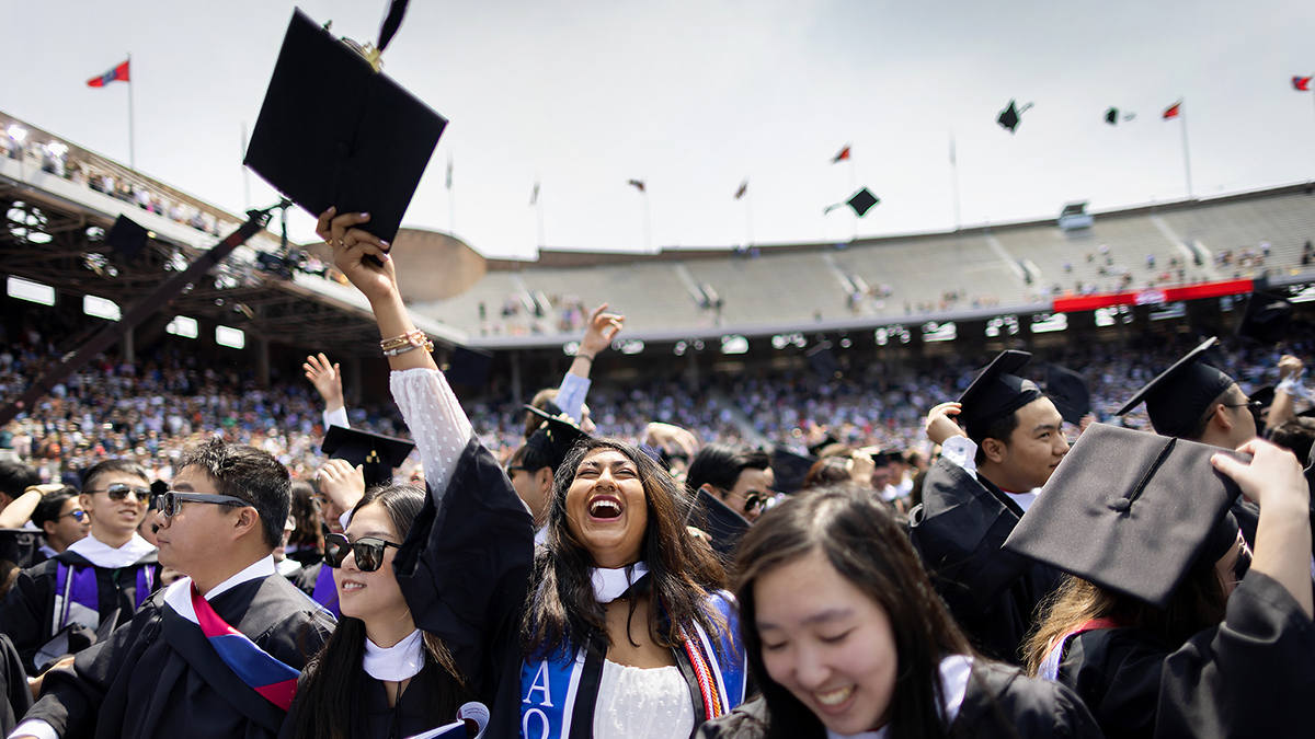 smiling graduates tossing caps on franklin field