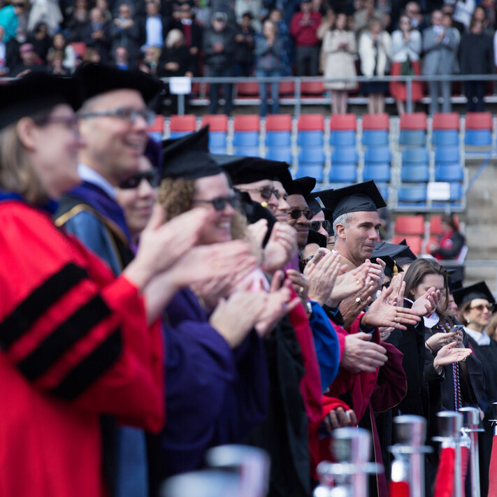 Penn faculty in regalia standing and clapping in Franklin Field